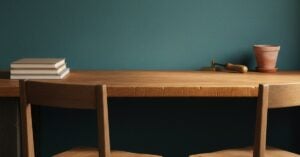 A stack of closed blank workbooks set aside on a worn oak workbench, the benchtop clear and lit, two wooden chairs angled toward each other